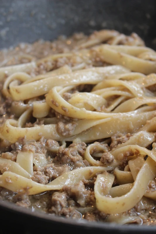 鍋の中で煮えているラグーと平打ちパスタ